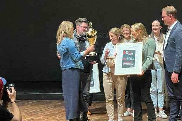 Eine Frau überreicht den Sieger-Pokal an eine Gruppe Frauen und Männer.