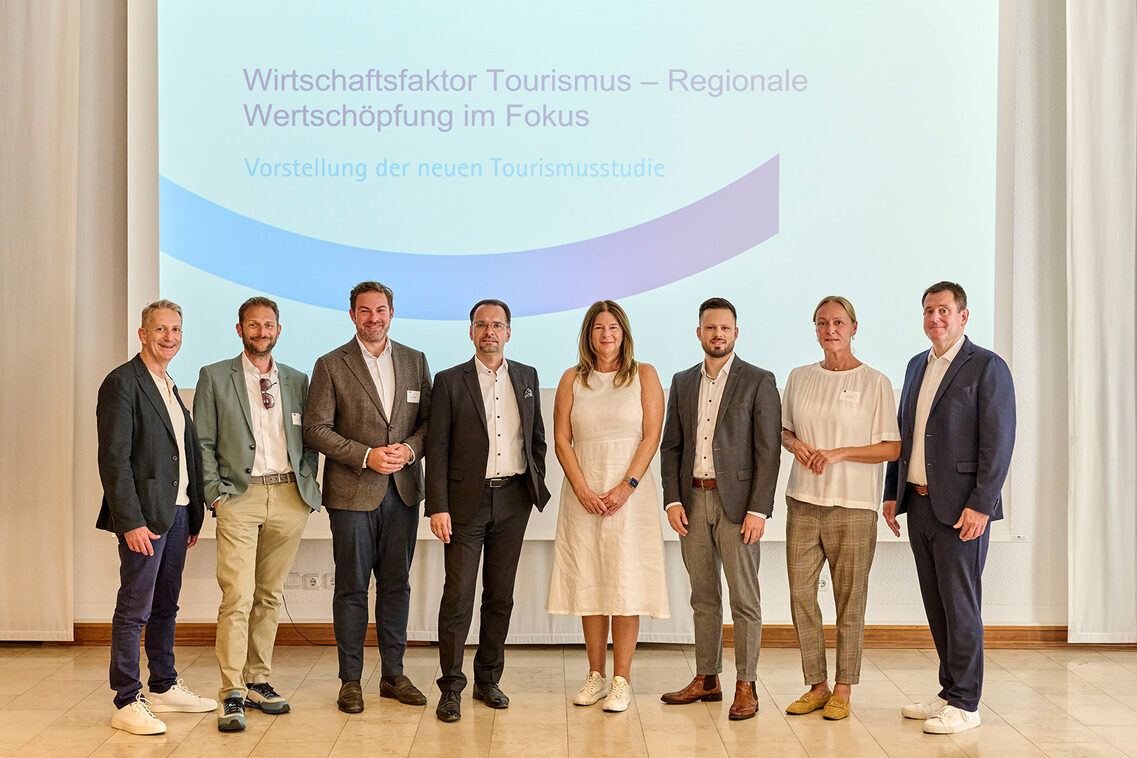 Sechs Männer und zwei Frauen vor einer Wand mit Slogan.